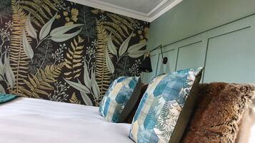 A bedroom with a bed, pillows, a wall with a leaf pattern, and a hanging lamp.