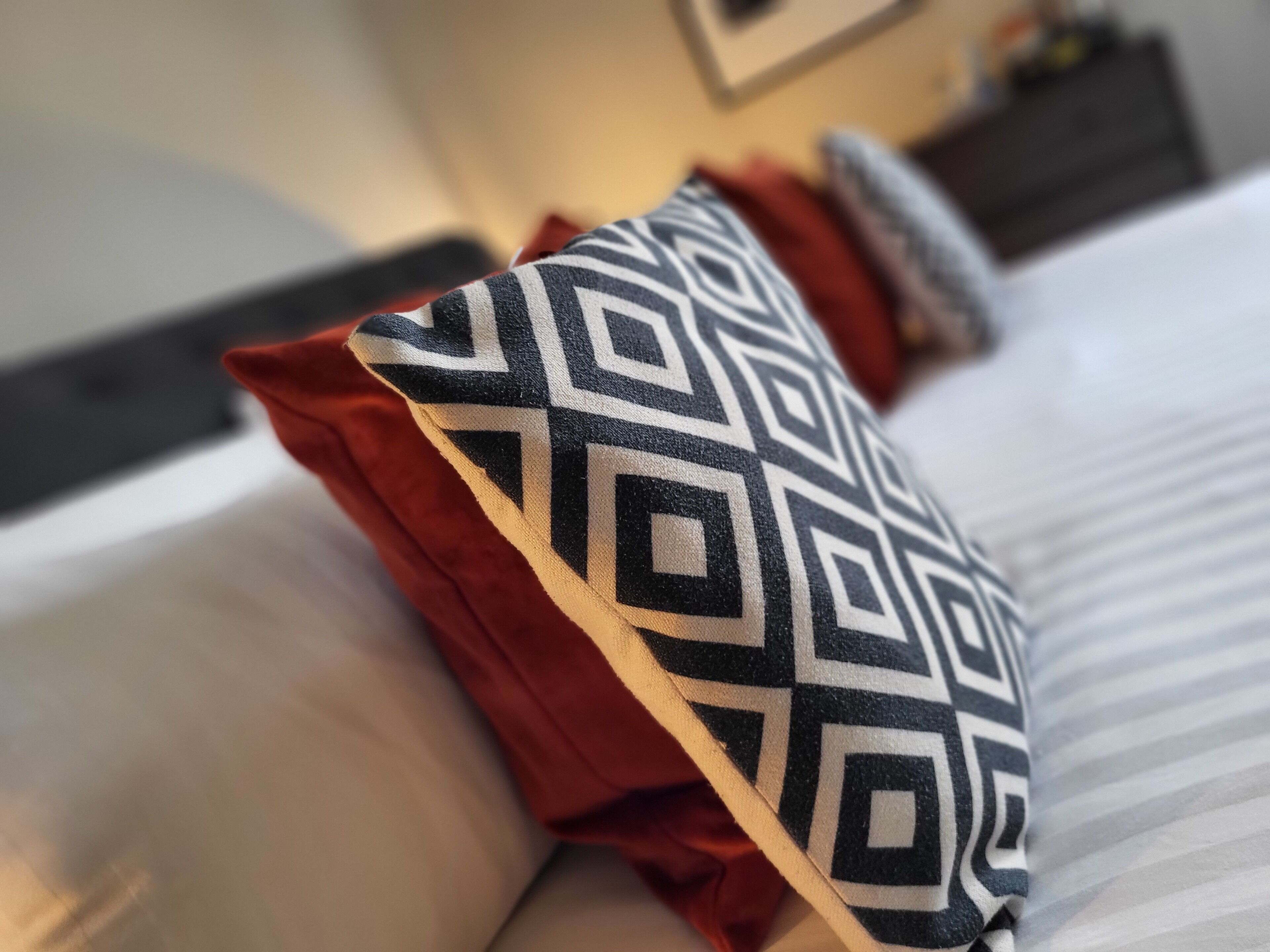 A bed with a patterned pillow and a red accent pillow.