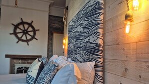 Una cama con almohadas estampadas, una rueda de barco en la pared y paneles de madera.