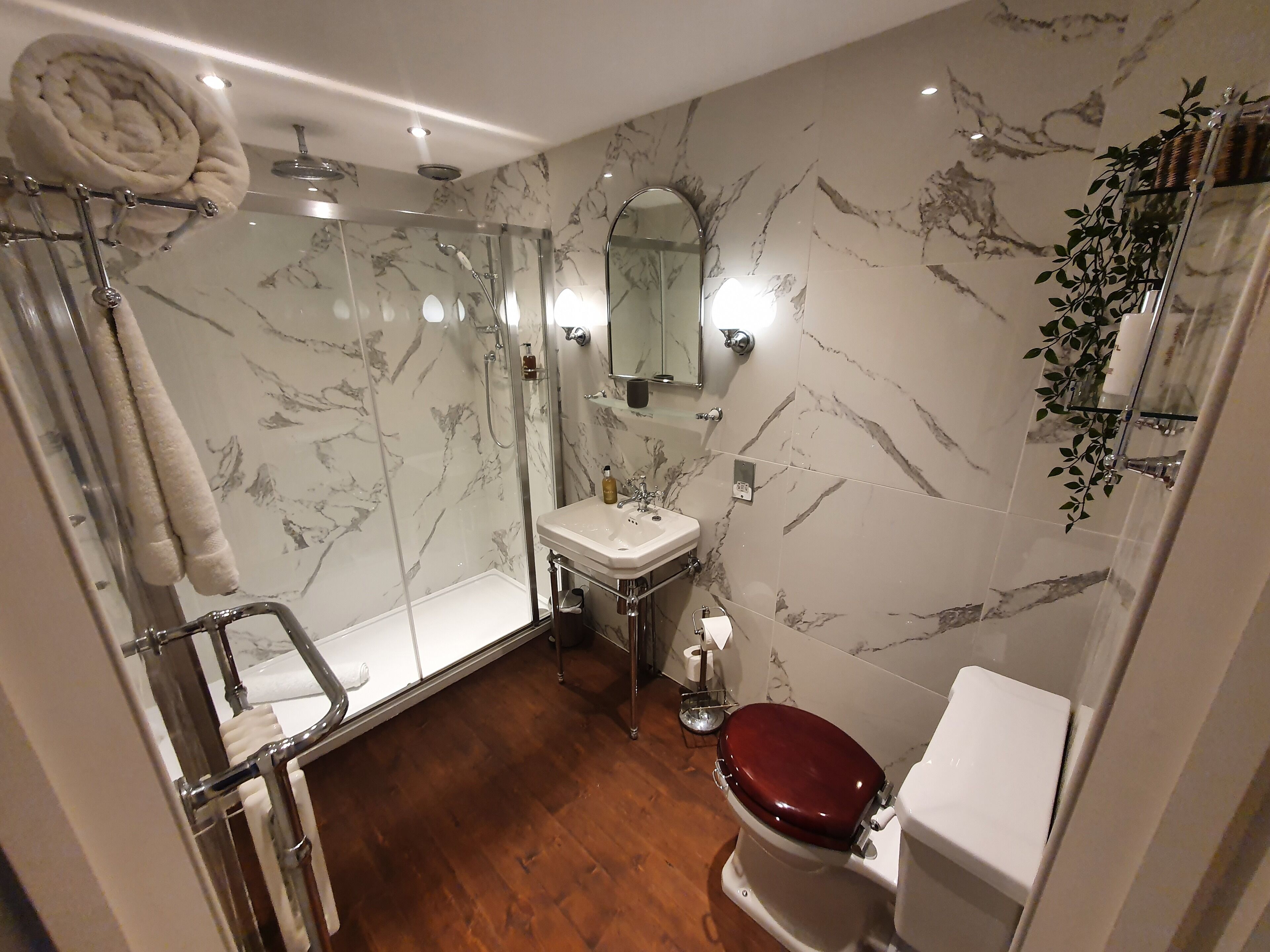A bathroom with a glass-enclosed shower, a white sink, a toilet, and marble-patterned walls.