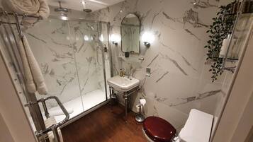 A bathroom with a glass-enclosed shower, a white sink, a toilet, and marble-patterned walls.