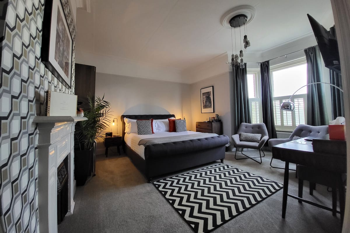Una habitación de hotel moderna con una cama grande, un escritorio con silla, una chimenea y vistas al exterior.
