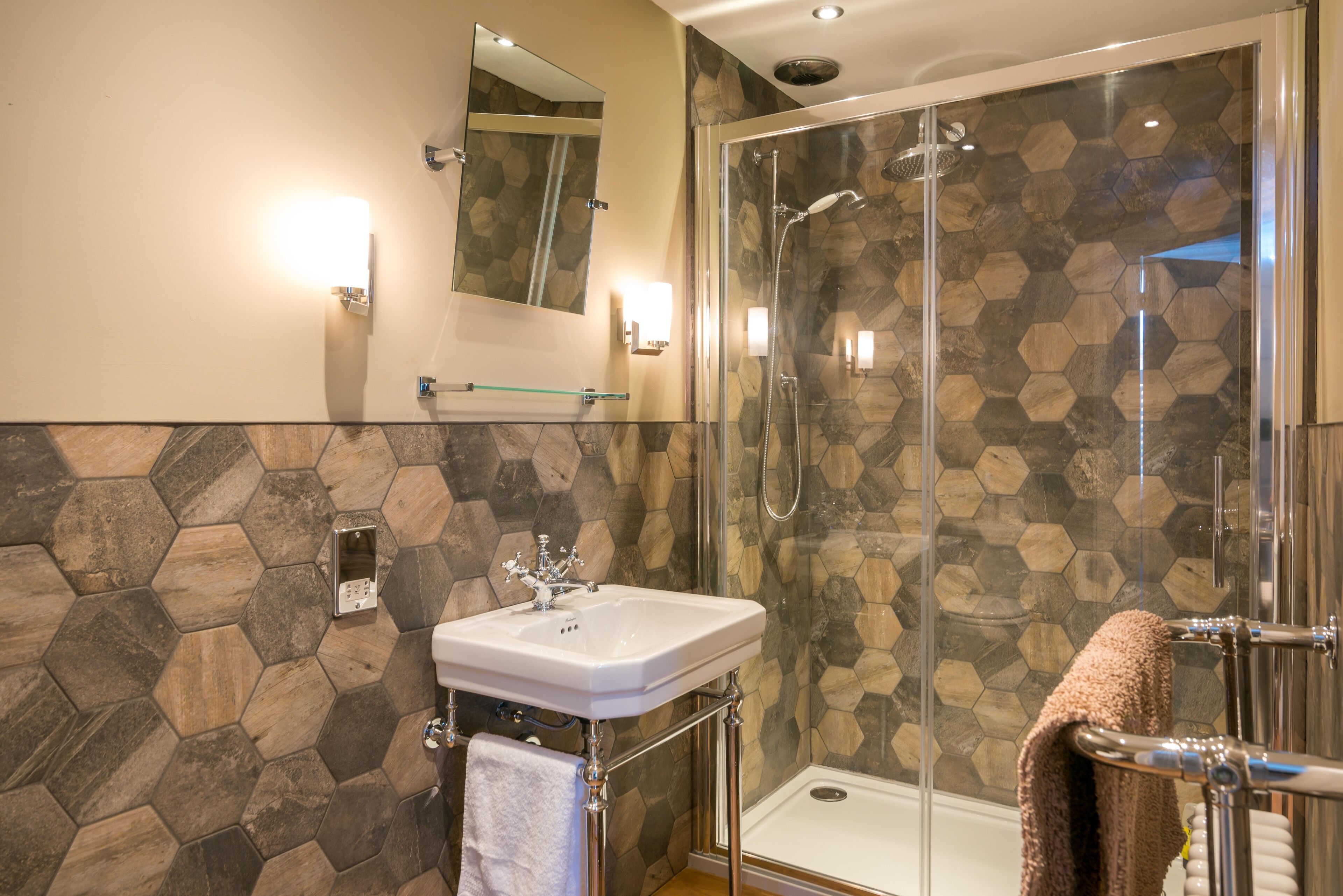 A modern bathroom with a glass-enclosed shower, a white sink, and a hexagonal tile backsplash.