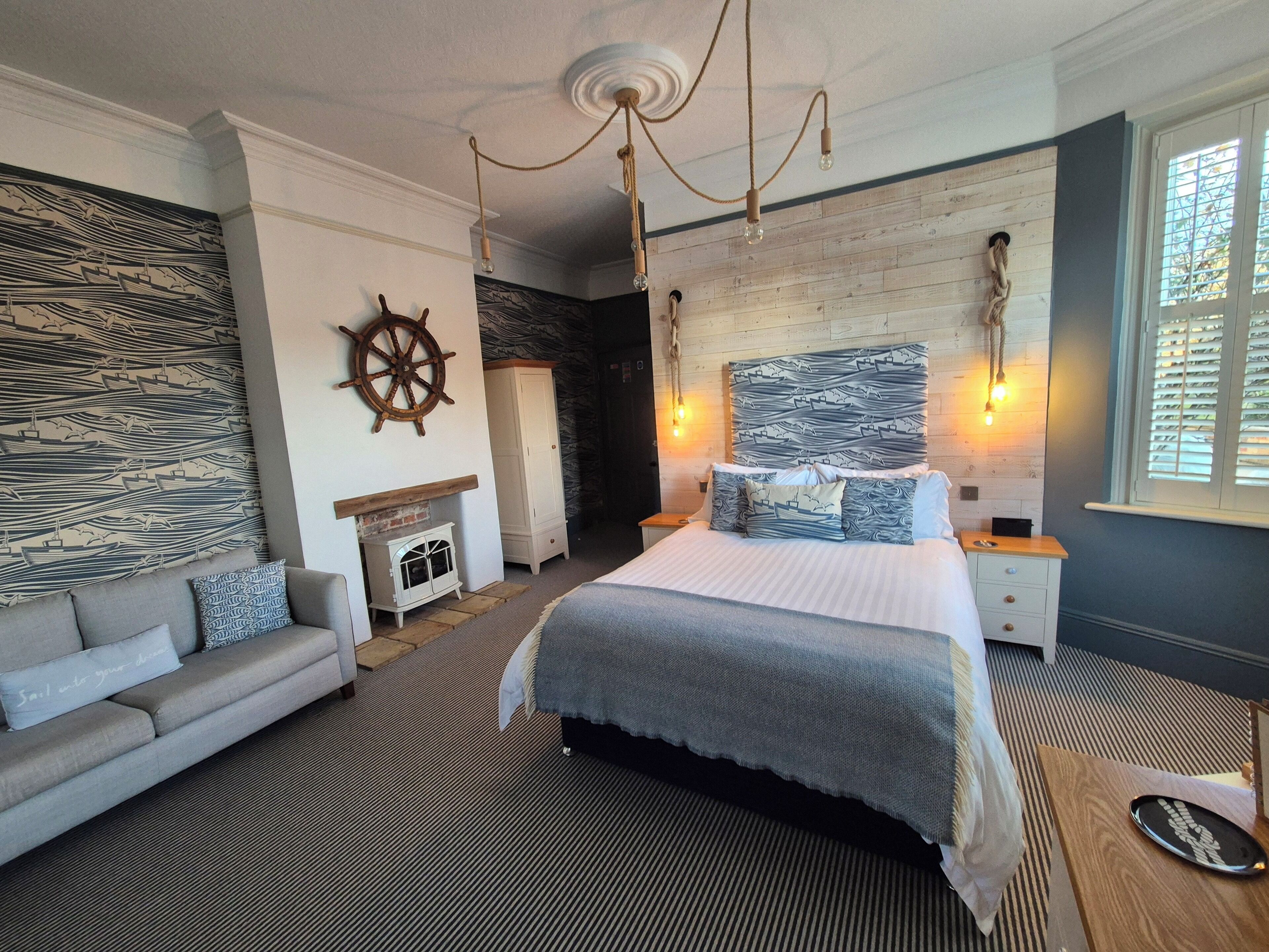 Un dormitorio con cama, sofá, cabecera de madera, timón de barco y chimenea.