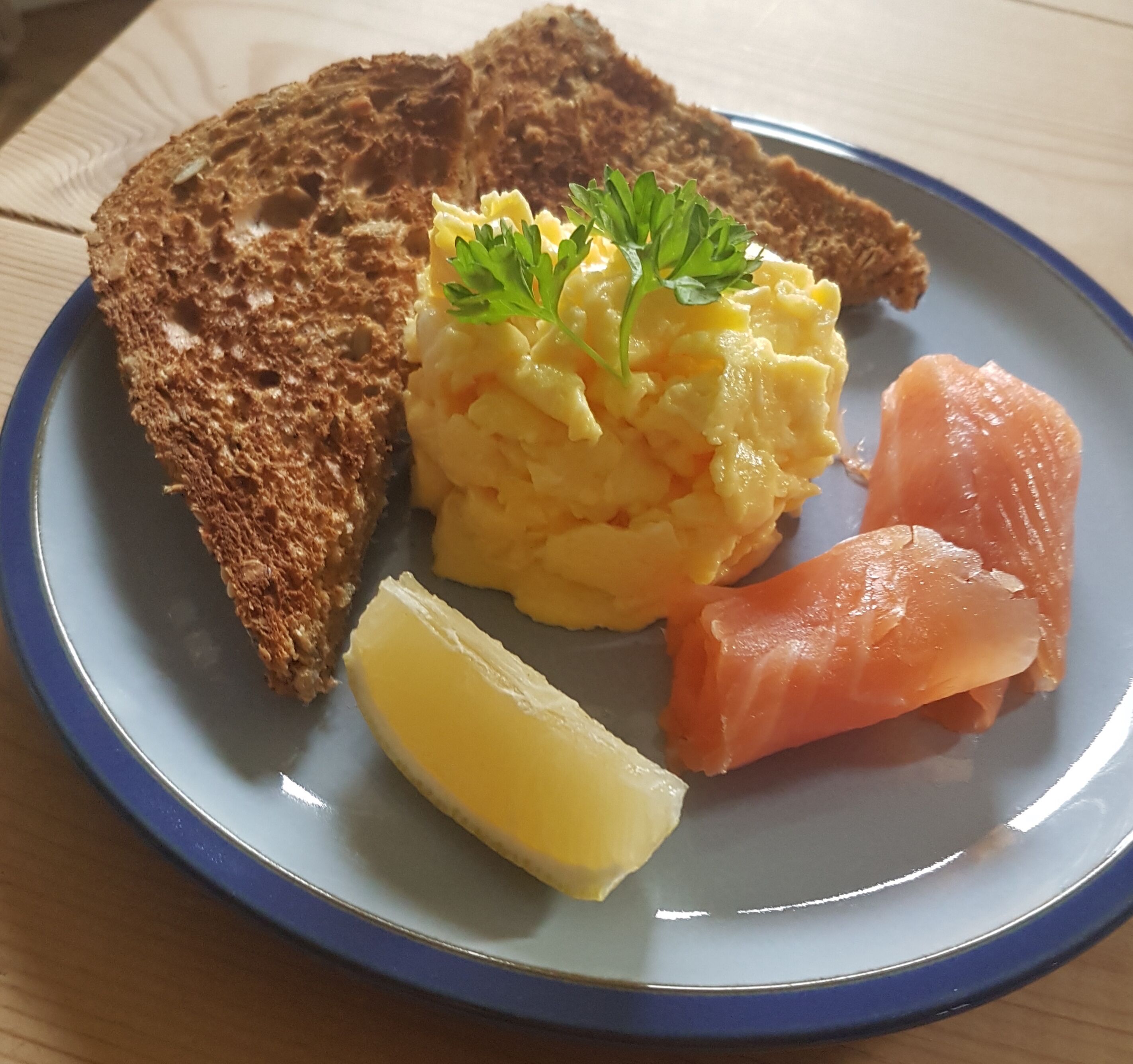 Une assiette contenant des œufs brouillés, du saumon fumé, une tranche de pain et un quartier de citron.