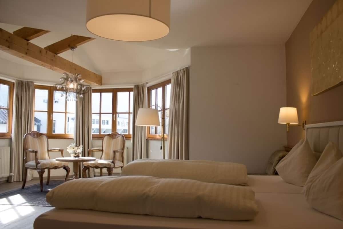 A hotel room with a bed, two chairs, a table, and a chandelier.