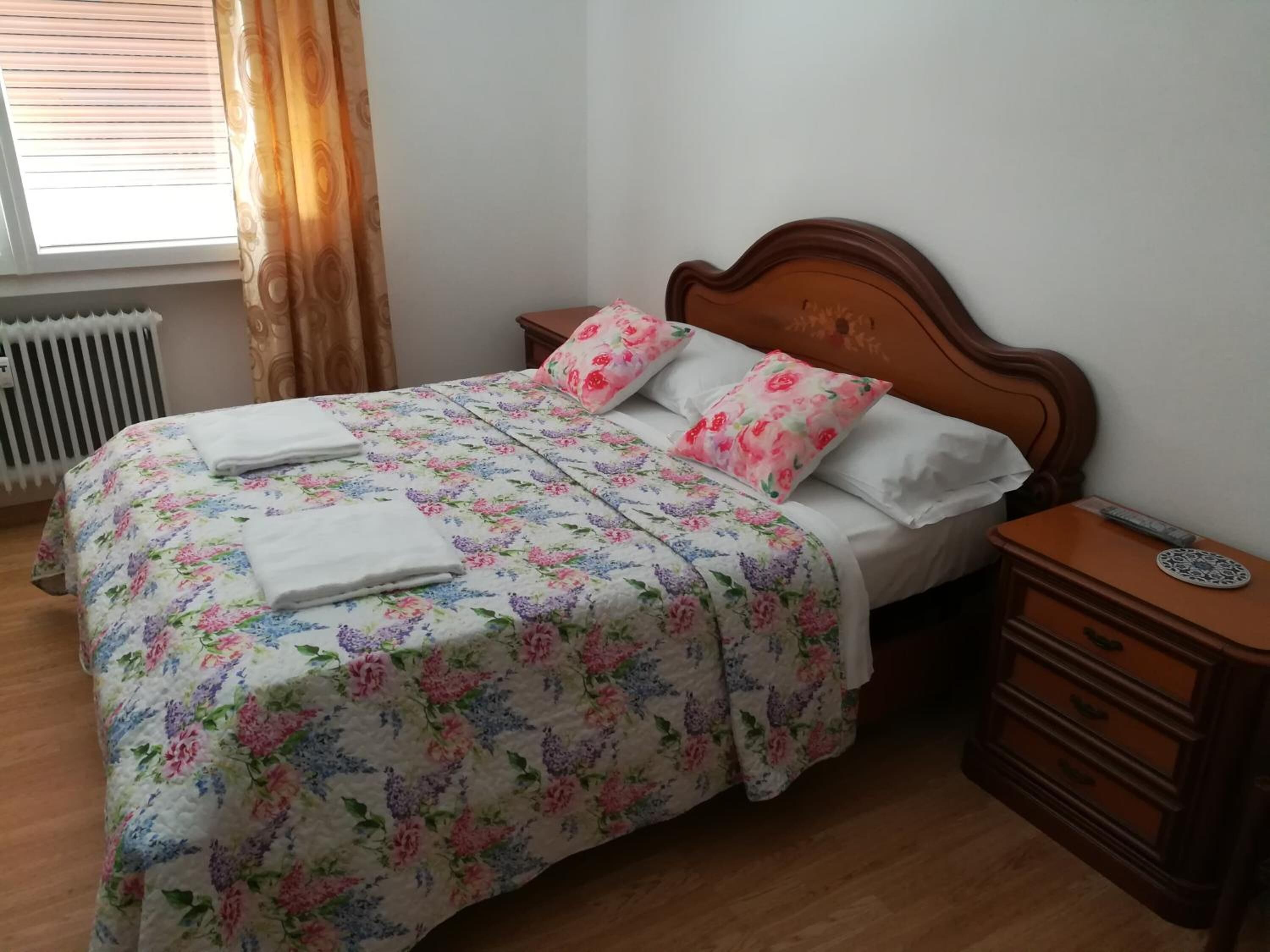 Una cama bien hecha con ropa de cama floral, un cabecero de madera y una mesita de noche con cajones.