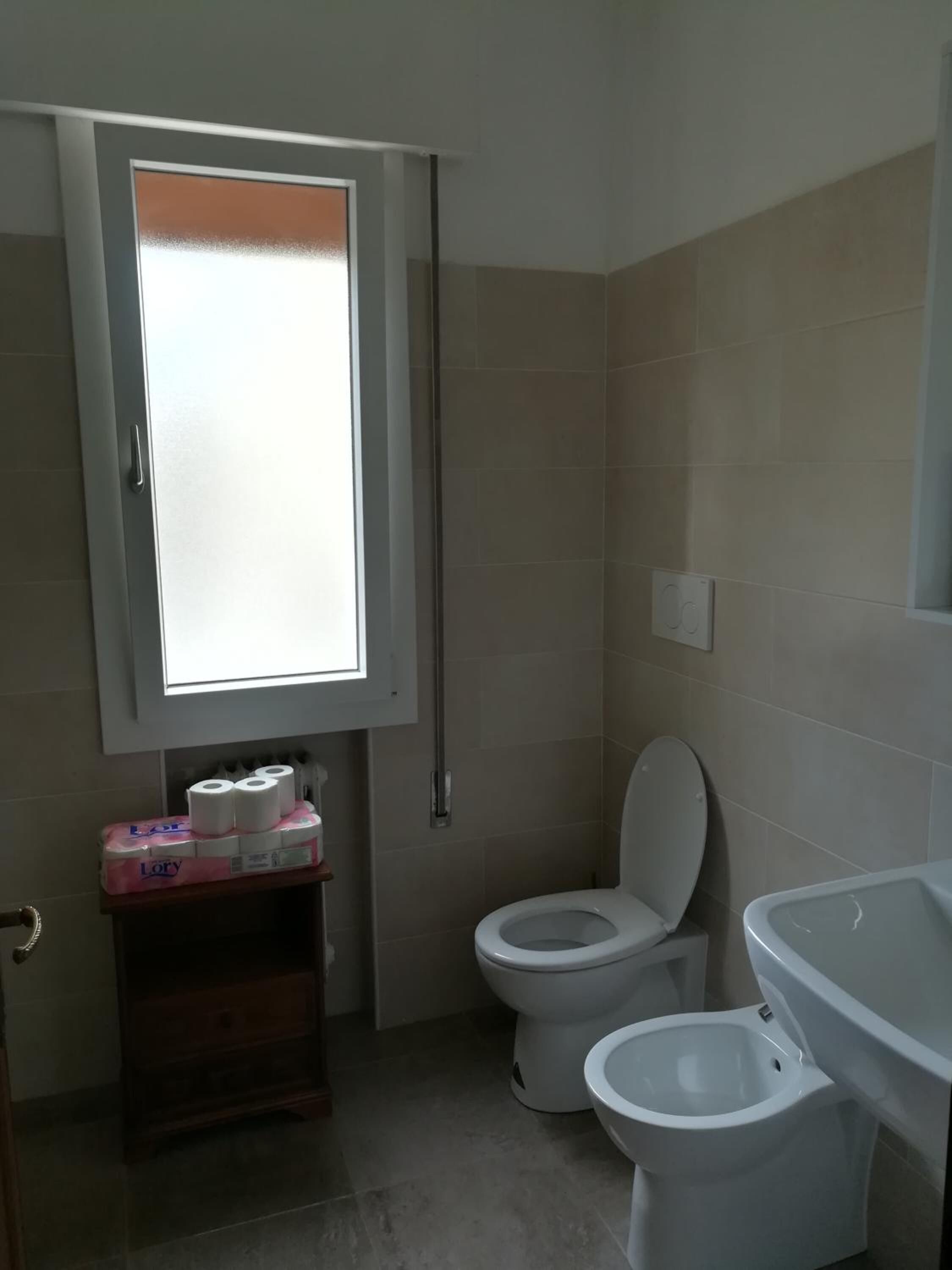 A bathroom with two toilets, a sink, and a window with frosted glass.