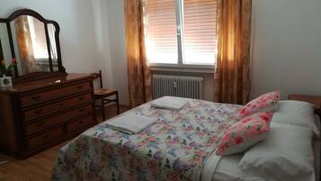 A bedroom with a wooden dresser, a bed with floral bedding, and a window with curtains.