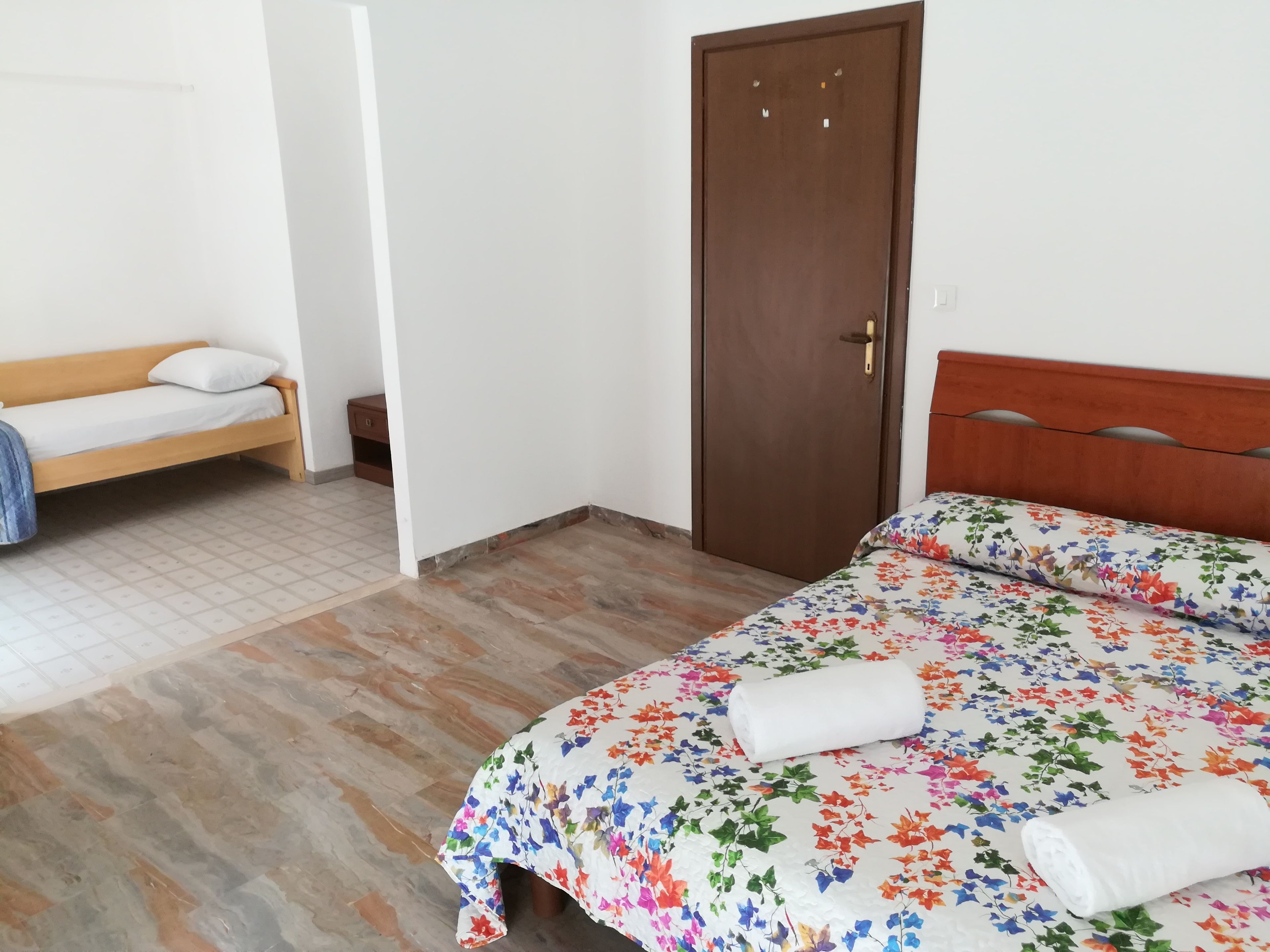 Una habitación con una cama, un banco, una puerta y una mesita.