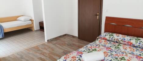 Una habitación con una cama, un banco, una puerta y una mesita.