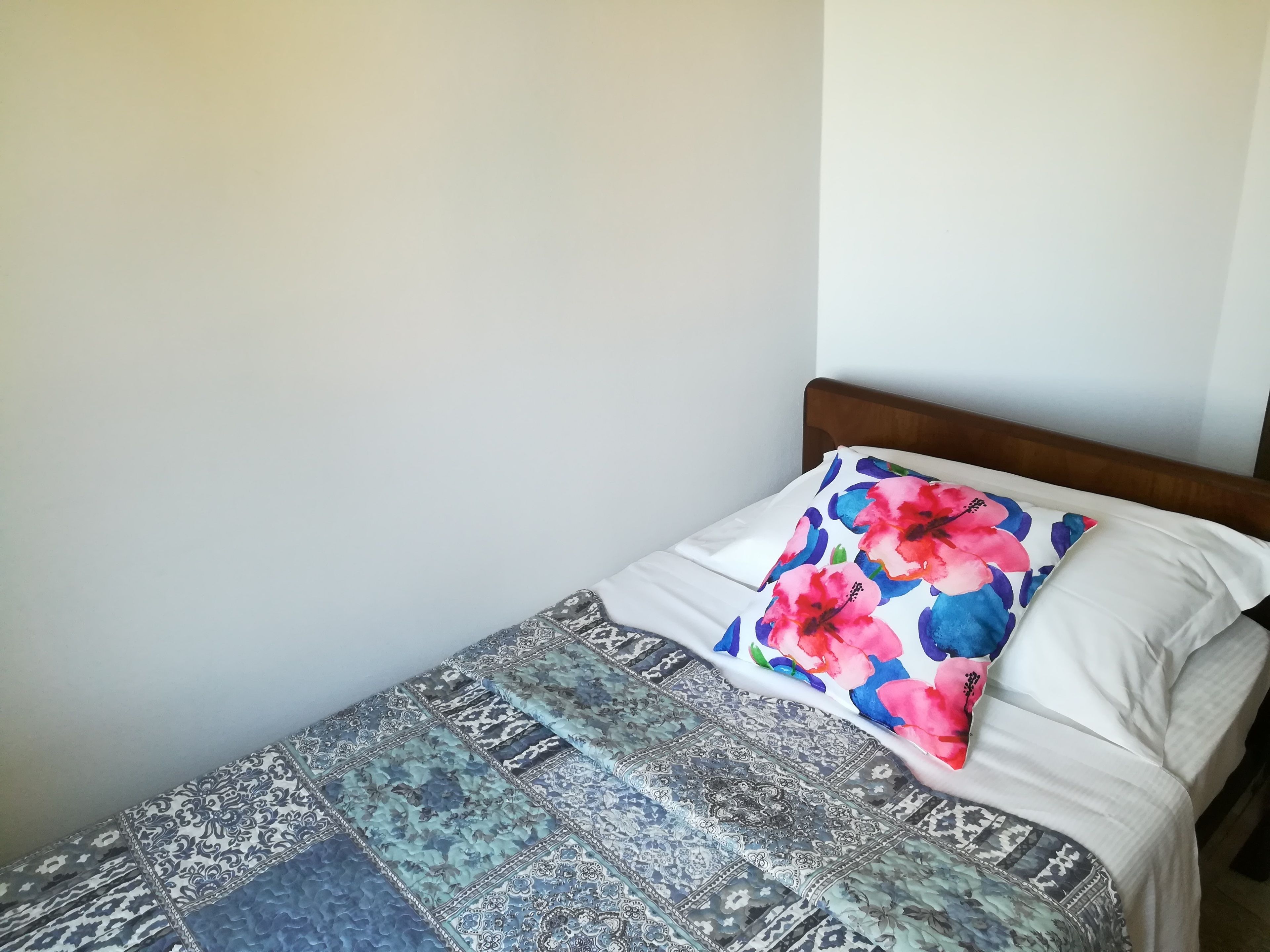 A bed with a patterned bedspread and two pillows, one with a floral design.