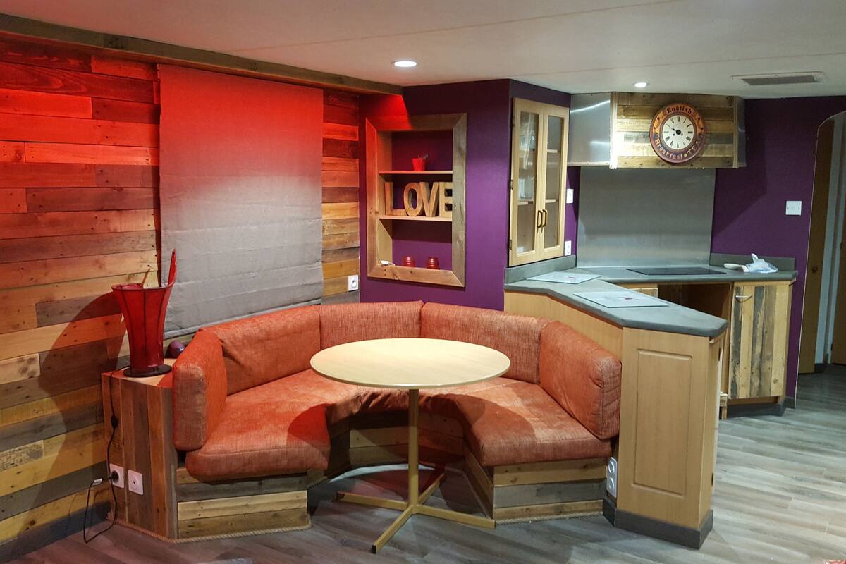 A compact kitchen with a built-in orange sofa and a small round table.