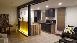 A modern kitchen with dark cabinets, a wooden island, and a dining area with a table and chairs. - Des Branches & Vous (Chateauneuf-sur-Isere)