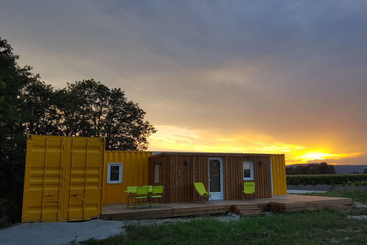 A small wooden cabin with a deck and two green chairs, set against a sunset backdrop.