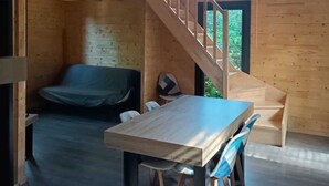 A wooden interior with a dining table, chairs, a sofa, a staircase, and a clock on the wall. - Des Branches & Vous (Chateauneuf-sur-Isere)