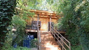 A wooden staircase leading to a cabin with a balcony, surrounded by dense greenery. - Des Branches & Vous (Chateauneuf-sur-Isere)