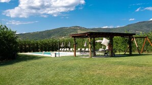 A pool area with a pergola, lounge chairs, and a view of hills. - Fattoria del Nonno Berto (Cortona)