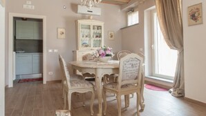 A dining area with a round table, four chairs, a chandelier, a cabinet with glass doors, and a window with curtains. - Fattoria del Nonno Berto (Cortona)