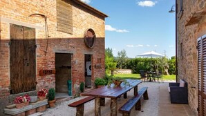 A rustic outdoor patio with a wooden table and benches, surrounded by potted plants and a brick building. - Fattoria del Nonno Berto (Cortona)
