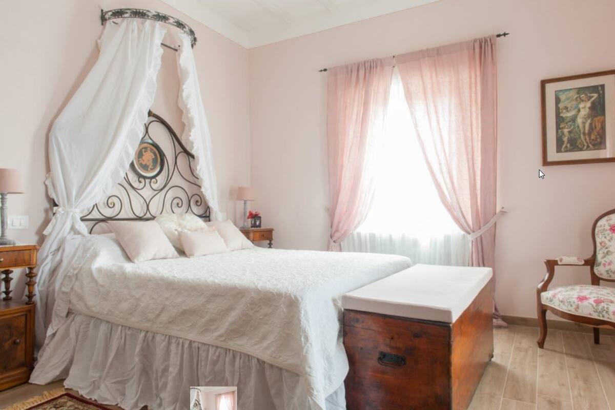 Une chambre à coucher avec un lit à baldaquin, une commode en bois, une chaise et une fenêtre avec des rideaux.