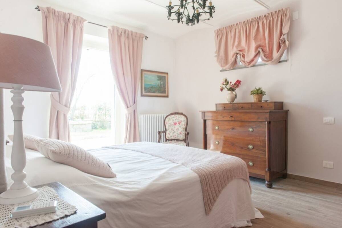 Une chambre à coucher comprenant un lit, une table de chevet, une commode, une chaise et une fenêtre avec des rideaux.
