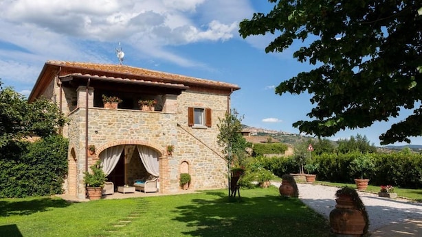 A stone building with a tiled roof, a covered patio, and a garden with potted plants. - Fattoria del Nonno Berto (Cortona)