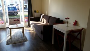 A living room with a sofa, a small table, and a chair. There is a window with a view of the outside. - 1 Sterling Court City Center (Canterbury)