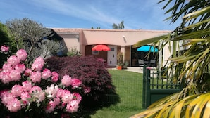 Una casa con puerta roja, un jardín con flores rosadas y una palmera.