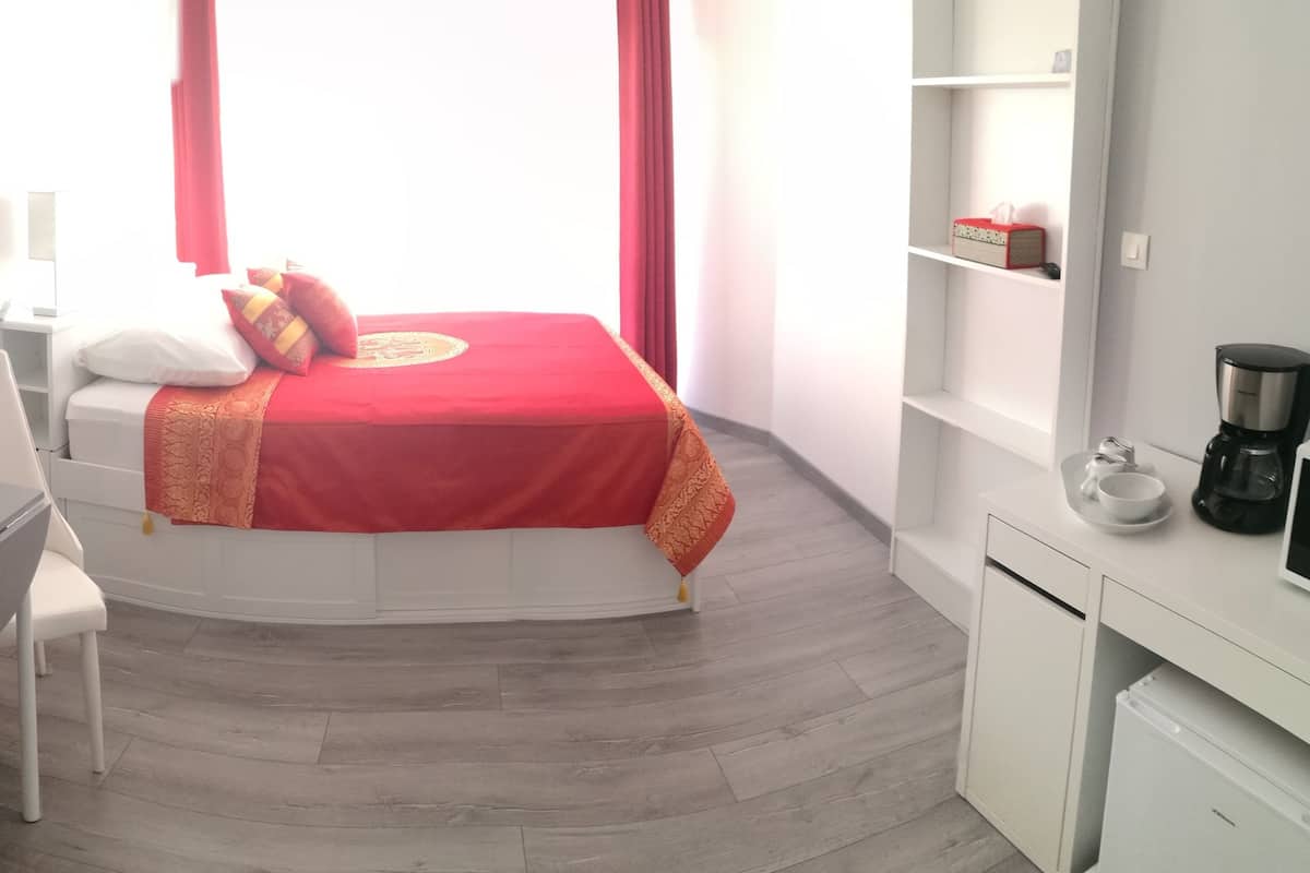 A small, modern room with a bed, a desk, a chair, a coffee maker, and a TV.
