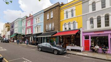 A street with colorful buildings, a parked car, and people sitting outside a shop.