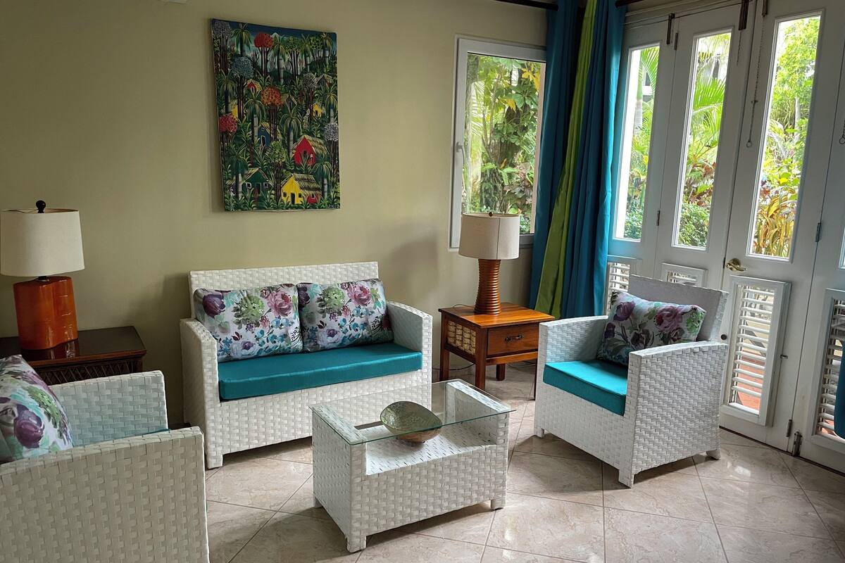 Ein Wohnzimmer mit einem weißen Sofa, zwei weißen Sesseln, einem Glastisch und einem Gemälde an der Wand.