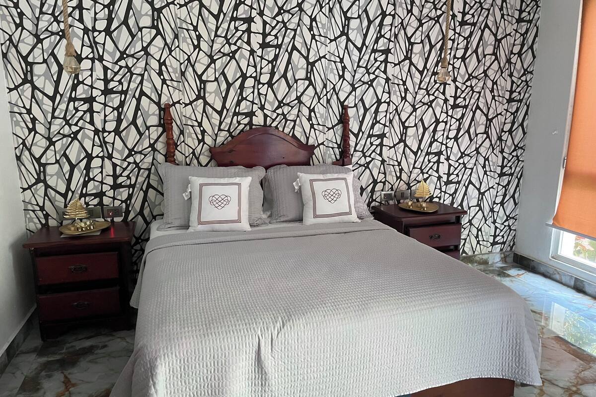 Ein Schlafzimmer mit einem Bett, einem Nachttisch, einer Kommode und einer Wand mit Muster.