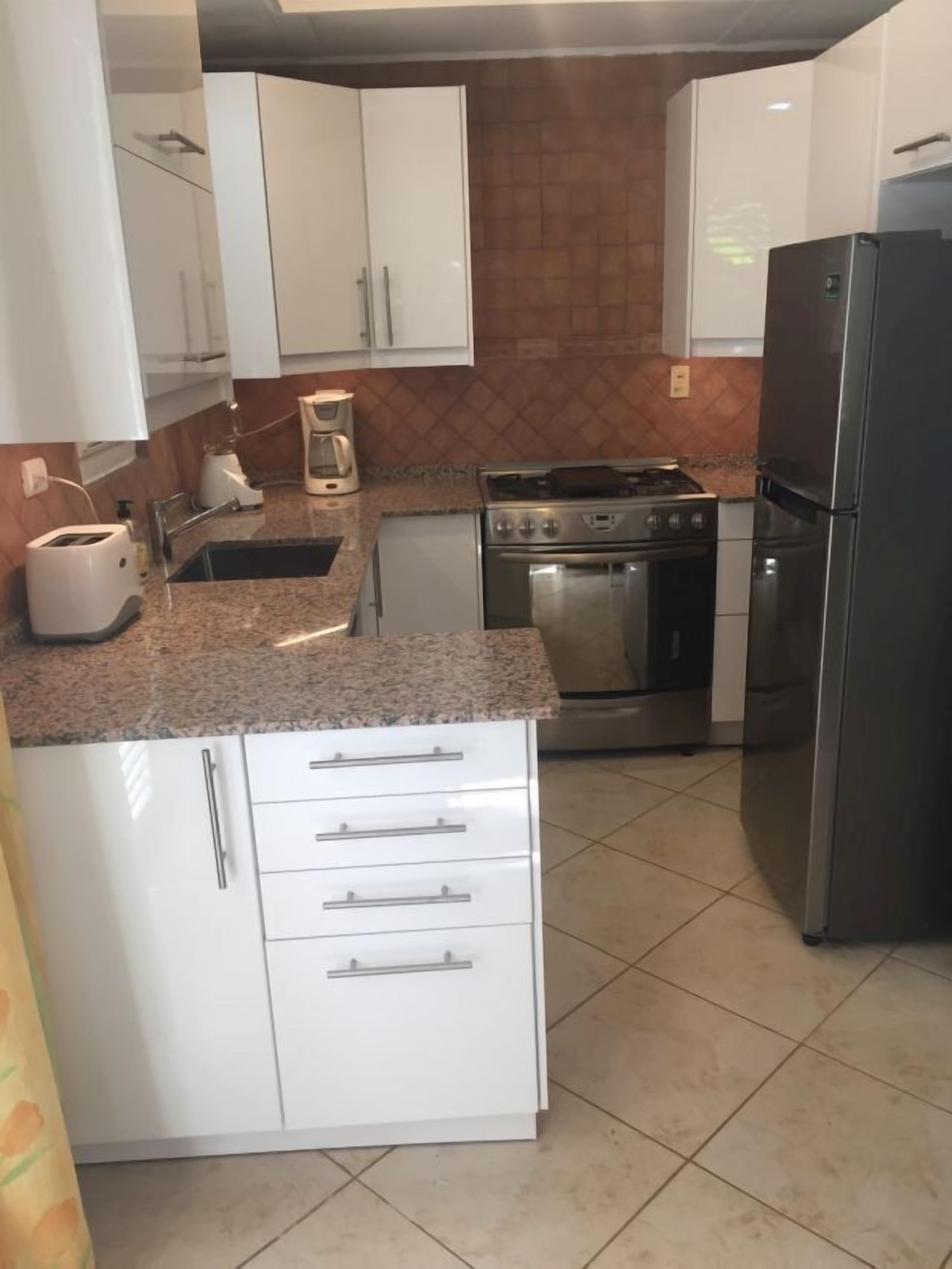 Eine Küche mit weißen Schränken, einem Herd, einem Backofen, einem Kühlschrank und einer Kaffeemaschine.