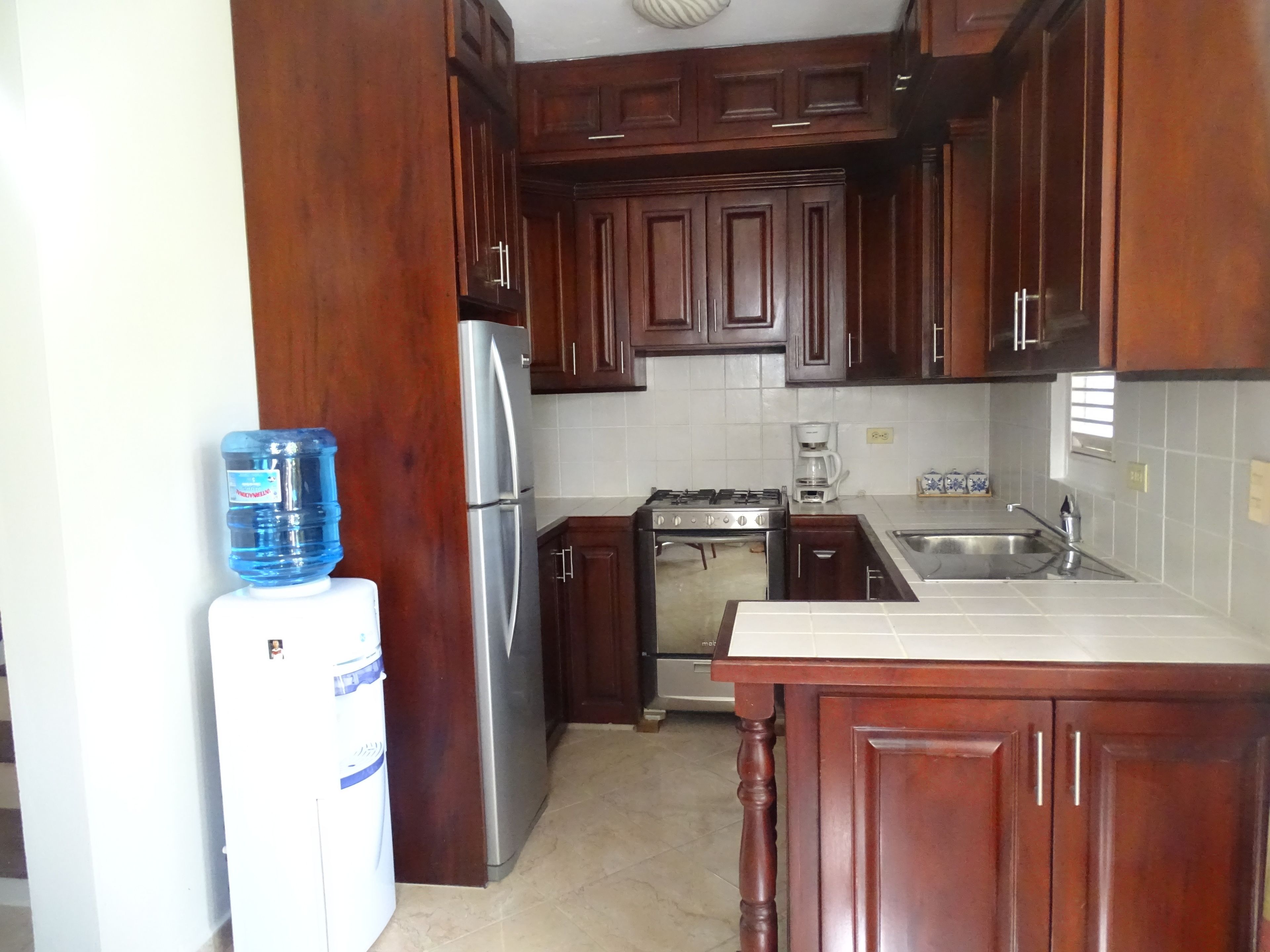 A kitchen with wooden cabinets, a stainless steel refrigerator, a gas stove, and a water dispenser.