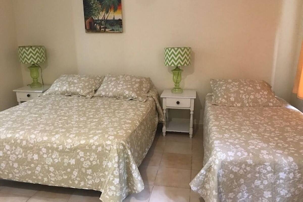 Ein Zimmer mit zwei Betten, jeweils mit einer blumigen Tagesdecke, zwei Nachttischen mit Lampen und einem Bild an der Wand.