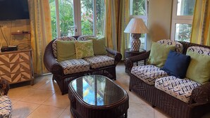 A living room with wicker furniture, a glass coffee table, and a TV on a wooden cabinet. - Albatros (Cabarete)