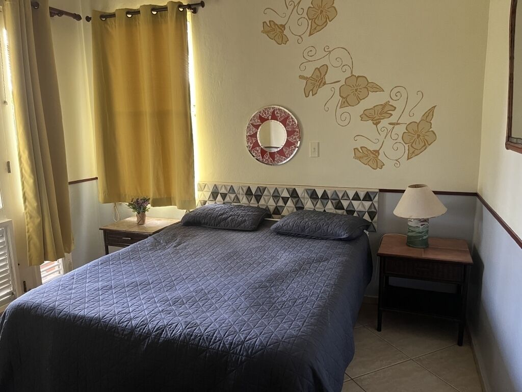 A bedroom with a bed, two bedside tables, a lamp, a wall clock, and a decorative wall piece.