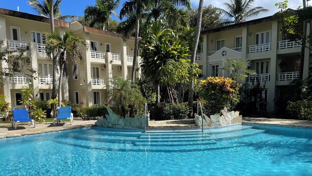 A clear swimming pool with blue water, surrounded by a stone border and palm trees. - Albatros (Cabarete)