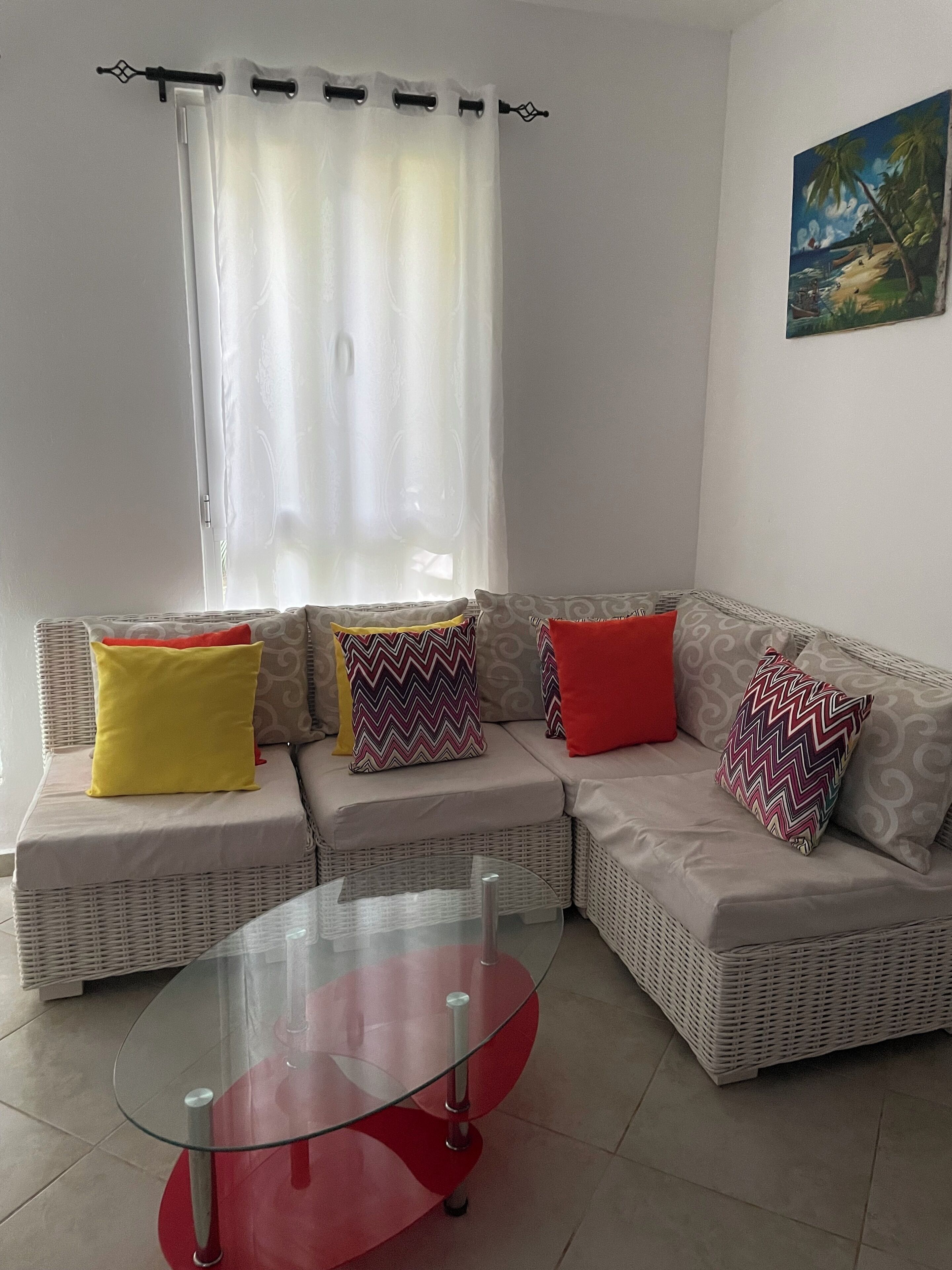 A living room with a sectional sofa, a glass coffee table, and a painting on the wall.