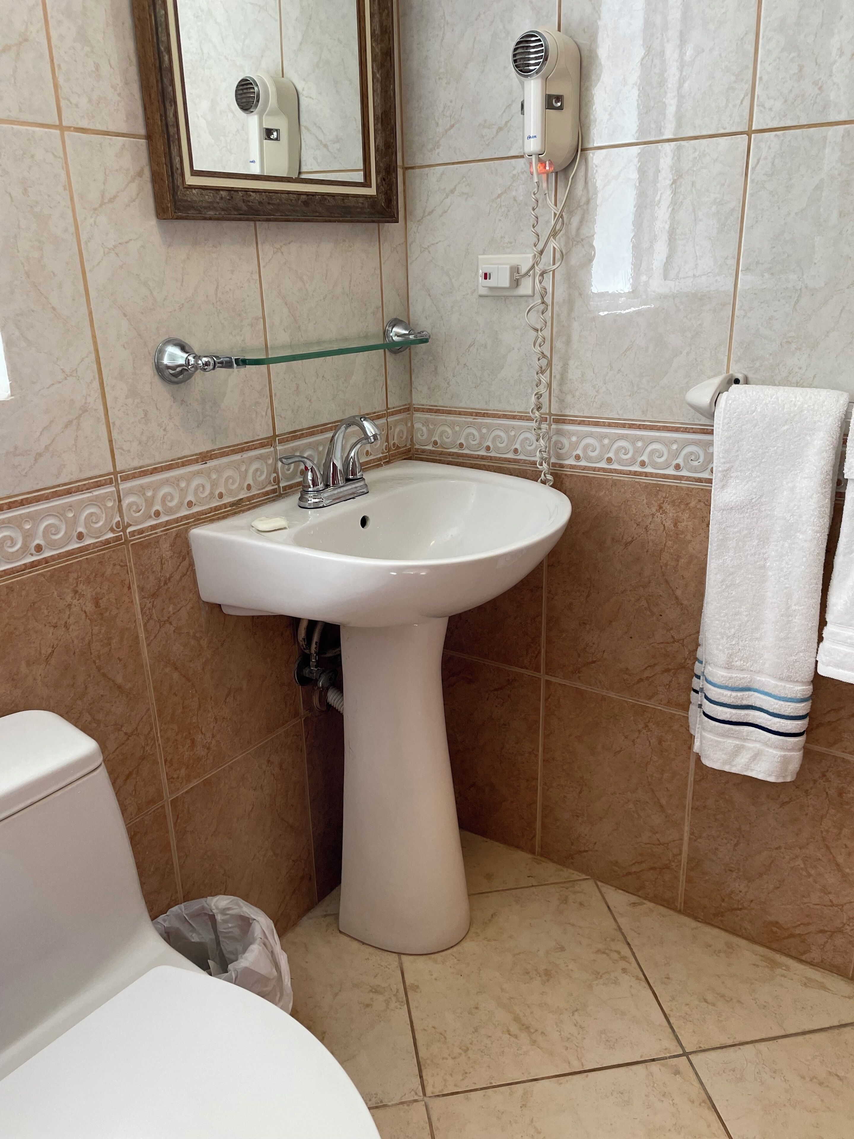 Une salle de bain équipée d’un lavabo sur colonne, d’un miroir, d’un sèche-cheveux et d’un porte-serviettes.