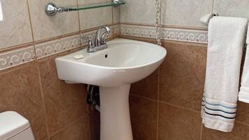 Une salle de bain équipée d’un lavabo sur colonne, d’un miroir, d’un sèche-cheveux et d’un porte-serviettes.
