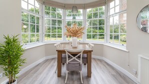 A corner room with a bay window, a dining table with chairs, a potted plant, and a hanging light fixture. - 3 Feversham House · Spacious 1-Bed Apartment in the Heart of York- Pass the Keys (York)