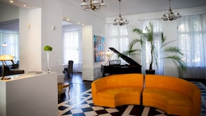 Una sala de estar moderna con piso de cuadros, un sofá naranja brillante, un piano de cola y un ventanal con cortinas translúcidas.