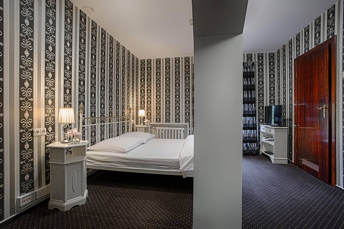 A hotel room with a bed, bedside tables, a wardrobe, and a television.