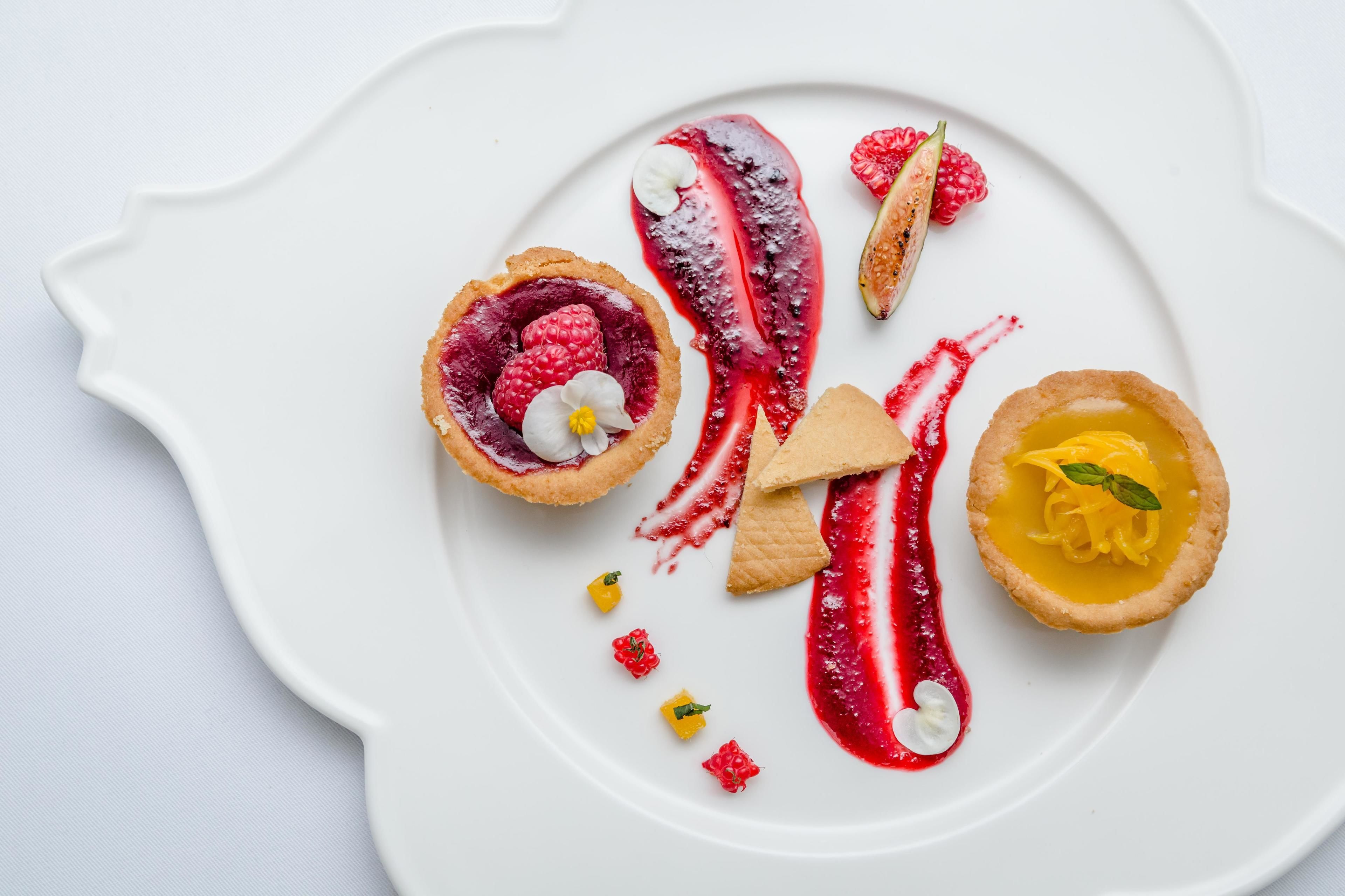 A white plate with various desserts, including a tart with raspberries and a yellow tart with a mint leaf.