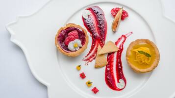 A white plate with various desserts, including a tart with raspberries and a yellow tart with a mint leaf.