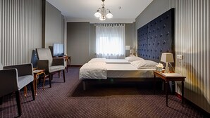 Una habitación de hotel con una cama grande, dos sillones, un escritorio, un televisor y una araña.