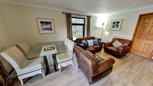 A living room with a glass table, leather sofas, and a wooden door. - Beautiful 4 star 2 bedroom chalet with stunning loch and mountain views (Crianlarich)