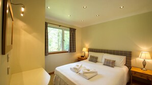A bedroom with a bed, two bedside lamps, a window with curtains, a bedside table, and a mirror. - Beautiful 4 star 2 bedroom chalet with stunning loch and mountain views (Crianlarich)